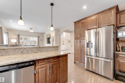 The kitchen features a stainless steel refrigerator, wood cabinetry, and granite countertops - 6002 46 Avenue, Beaumont, AB - Indoor Photo Showing Kitchen