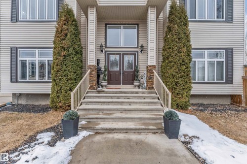 The property features a welcoming entrance with concrete steps and railings, flanked by tall evergreen shrubs - 6002 46 Avenue, Beaumont, AB - Outdoor With Facade