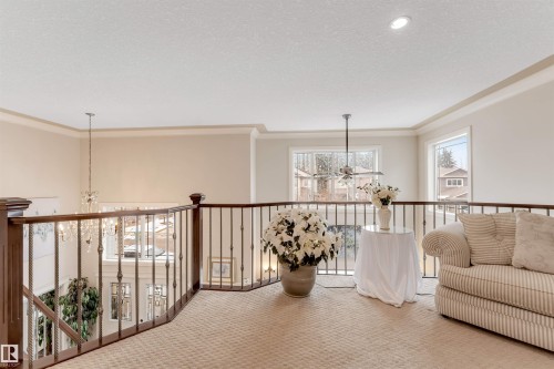 This property features an inviting upper landing with carpeted flooring, a sturdy wood and metal railing, and ample natural light from the windows - 6002 46 Avenue, Beaumont, AB - Indoor Photo Showing Other Room