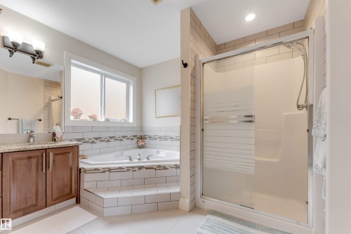 The bathroom features a built-in tub with tile surround, a separate shower with a glass enclosure, and a vanity with a granite countertop - 6002 46 Avenue, Beaumont, AB - Indoor Photo Showing Bathroom