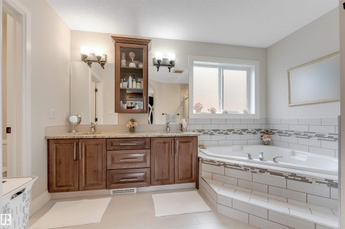Bathroom featuring a dual vanity with a granite countertop, a built-in jetted tub with tiled surround, and a window providing natural light - 6002 46 Avenue, Beaumont, AB - Indoor Photo Showing Bathroom