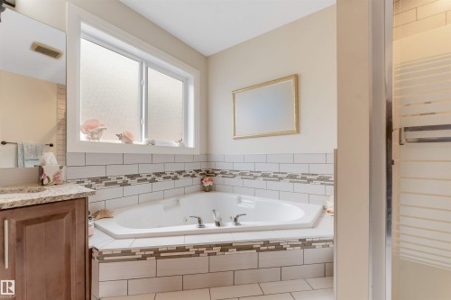 Bathroom featuring a built-in corner tub with tiled surround, a vanity with granite countertop, and a shower enclosure - 6002 46 Avenue, Beaumont, AB - Indoor Photo Showing Bathroom