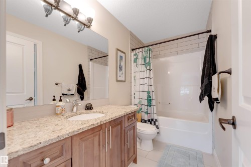 The bathroom features a vanity with a light-colored granite countertop and a white sink, a mirror, and a light fixture with four bulbs - 6002 46 Avenue, Beaumont, AB - Indoor Photo Showing Bathroom