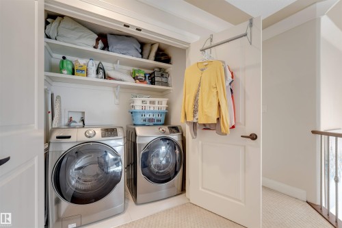 Dedicated laundry area featuring a front-loading washing machine and dryer, built-in shelving, and a hanging rod - 6002 46 Avenue, Beaumont, AB - Indoor Photo Showing Laundry Room