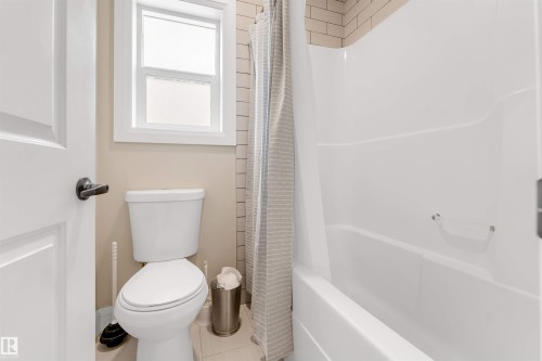 The bathroom features a white toilet, a white bathtub with an integrated shower, and a window with white trim - 6002 46 Avenue, Beaumont, AB - Indoor Photo Showing Bathroom
