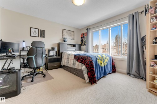 This room features a large window with views of the surrounding neighborhood, light-colored carpeting, and a built-in bed frame with drawers - 6002 46 Avenue, Beaumont, AB - Indoor Photo Showing Bedroom