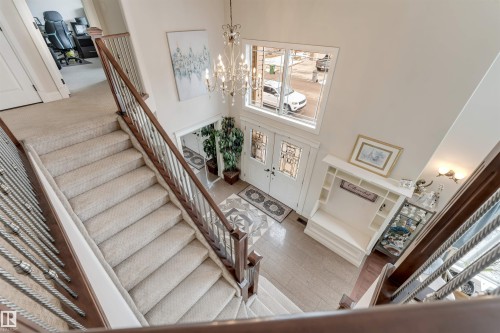 Foyer with double entry doors featuring decorative glass, a grand staircase with carpeted treads and wrought iron railings, and a chandelier - 6002 46 Avenue, Beaumont, AB - Indoor Photo Showing Other Room