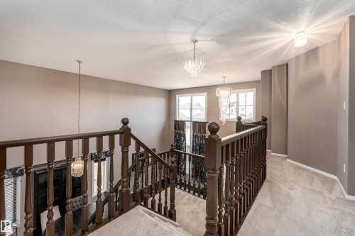 Upper-level landing featuring wood balustrade, neutral carpeting, and multiple crystal chandeliers - 8407 160 Avenue, Edmonton, AB - Indoor Photo Showing Other Room