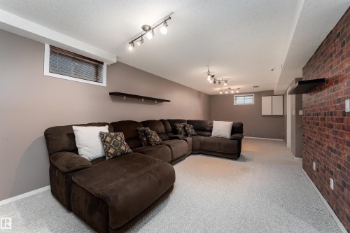 Finished lower-level space featuring track lighting, light gray carpet flooring, a window with blinds, and a partial exposed brick wall - 8407 160 Avenue, Edmonton, AB - Indoor