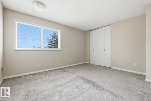 Carpeted room featuring a large window with horizontal blinds, a ceiling-mounted light fixture, and white bi-fold closet doors - 10640 Beaumaris Road, Edmonton, AB - Indoor Photo Showing Other Room