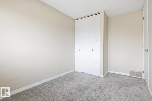 Neutral-toned walls complementing gray carpeting, white baseboards, and a white bi-fold closet with panel detailing - 10640 Beaumaris Road, Edmonton, AB - Indoor Photo Showing Other Room