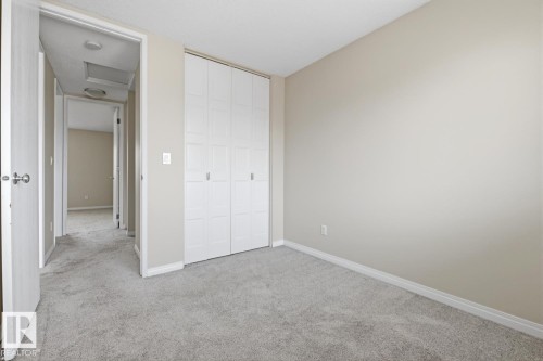 Neutral-toned room featuring light gray carpeting, white trim, and a full-wall bi-fold closet with white panel doors - 10640 Beaumaris Road, Edmonton, AB - Indoor Photo Showing Other Room