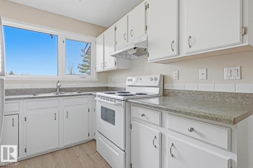 Kitchen featuring white cabinetry, a white electric range, wood-finish flooring, a stainless steel sink, and light-toned countertops - 10640 Beaumaris Road, Edmonton, AB - Indoor Photo Showing Kitchen With Double Sink