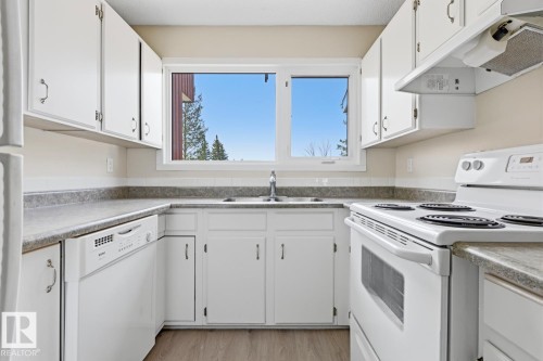 Bright kitchen featuring white cabinetry and appliances, laminate countertops, wood-finish flooring, and a large window above the sink - 10640 Beaumaris Road, Edmonton, AB - Indoor Photo Showing Kitchen With Double Sink