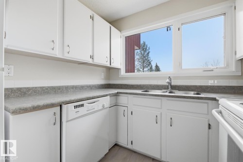 Kitchen featuring white cabinetry with brushed nickel hardware, a double basin stainless steel sink with a chrome faucet, and grey speckled countertops - 10640 Beaumaris Road, Edmonton, AB - Indoor Photo Showing Kitchen With Double Sink