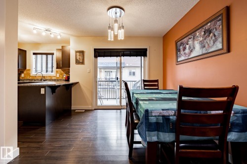 Dining area featuring dark wood flooring, a modern chandelier, and access to an outdoor balcony through a glass sliding door - 40 12004 22 Avenue, Edmonton, AB - Indoor Photo Showing Dining Room