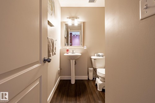 The bathroom features a pedestal sink with a mirror and vanity lighting, a toilet, and dark wood-style flooring - 40 12004 22 Avenue, Edmonton, AB - Indoor Photo Showing Bathroom