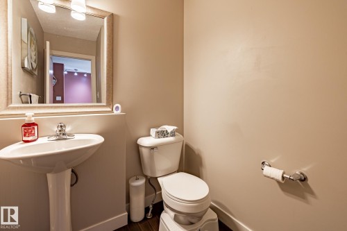 Bathroom featuring a pedestal sink with a chrome faucet, a toilet, a mirror with an ornate frame, and light-colored walls - 40 12004 22 Avenue, Edmonton, AB - Indoor Photo Showing Bathroom