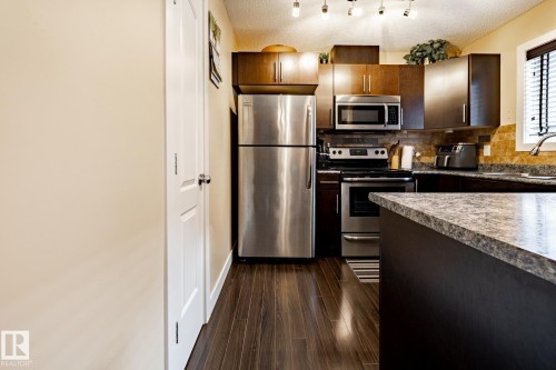 The kitchen features stainless steel appliances, dark wood cabinetry, a tiled backsplash, and stone countertops - 40 12004 22 Avenue, Edmonton, AB - Indoor Photo Showing Kitchen With Stainless Steel Kitchen