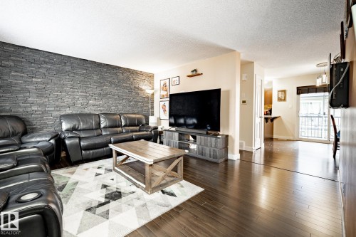 Living area featuring a stone veneer accent wall and dark wood-finish flooring - 40 12004 22 Avenue, Edmonton, AB - Indoor Photo Showing Living Room