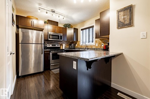 The kitchen features stainless steel appliances, dark wood cabinetry, and granite countertops - 40 12004 22 Avenue, Edmonton, AB - Indoor Photo Showing Kitchen With Stainless Steel Kitchen