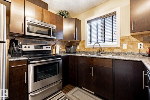 Kitchen featuring stainless steel appliances, dark wood cabinetry, a tiled backsplash, and a window with blinds above the sink - 40 12004 22 Avenue, Edmonton, AB - Indoor Photo Showing Kitchen With Stainless Steel Kitchen With Double Sink