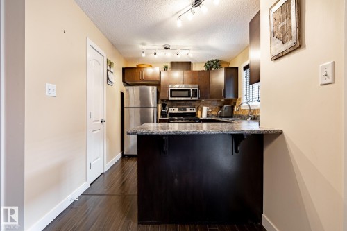 The kitchen features dark wood cabinetry, stainless steel appliances, and a granite countertop - 40 12004 22 Avenue, Edmonton, AB - Indoor Photo Showing Kitchen With Stainless Steel Kitchen With Upgraded Kitchen