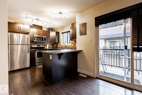 The kitchen features dark wood cabinetry, stainless steel appliances, and a granite-look island - 40 12004 22 Avenue, Edmonton, AB - Indoor Photo Showing Kitchen With Stainless Steel Kitchen