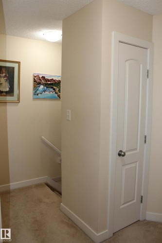Hallway featuring neutral carpet flooring, white baseboards, a white interior door, a staircase with a white handrail, and a flush-mount ceiling light fixture - 40 12004 22 Avenue, Edmonton, AB - Indoor Photo Showing Other Room