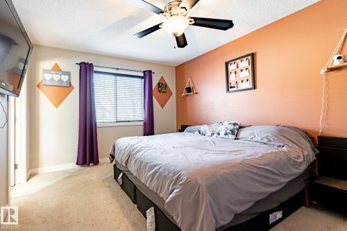 Spacious bedroom featuring warm-toned walls, textured ceiling, a window with horizontal blinds, and a ceiling fan with integrated lighting - 40 12004 22 Avenue, Edmonton, AB - Indoor Photo Showing Bedroom