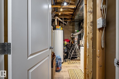 Utility area featuring a water heater, visible exposed ceiling joists, and exposed wiring - 40 12004 22 Avenue, Edmonton, AB - Indoor Photo Showing Basement