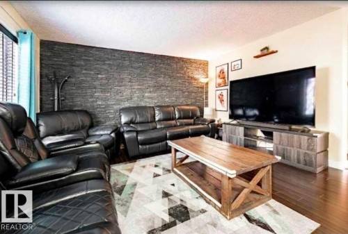 Living area featuring a floor-to-ceiling accent wall with textured stone-look paneling - 40 12004 22 Avenue, Edmonton, AB - Indoor Photo Showing Living Room