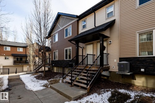 The property features an exterior with light-colored siding, a dark roof, and a covered porch entry - 40 12004 22 Avenue, Edmonton, AB - Outdoor