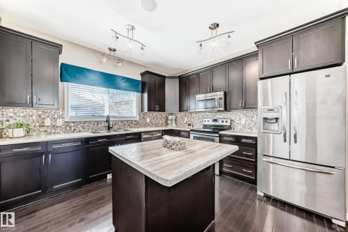 Expansive kitchen featuring dark wood cabinetry, a mosaic tile backsplash, and stainless steel appliances - 5020 Orchards Gate, Edmonton, AB - Indoor Photo Showing Kitchen With Stainless Steel Kitchen With Upgraded Kitchen