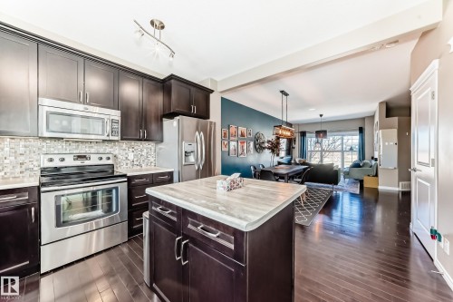 Kitchen featuring dark wood cabinetry, stainless steel appliances, a mosaic tile backsplash, and a central island with a light-toned countertop - 5020 Orchards Gate, Edmonton, AB - Indoor Photo Showing Kitchen With Stainless Steel Kitchen With Upgraded Kitchen