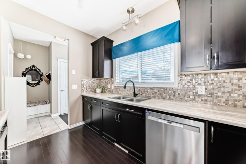 Contemporary kitchen featuring dark wood-finish cabinetry, stainless steel appliances, a mosaic tile backsplash, and light-toned countertops - 5020 Orchards Gate, Edmonton, AB - Indoor Photo Showing Kitchen With Double Sink