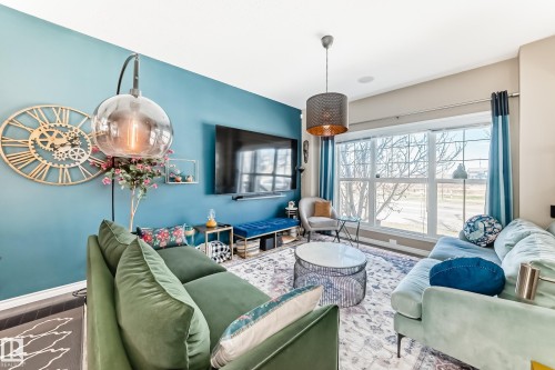 Spacious living area featuring a large window, a wall-mounted television, a contemporary ceiling light fixture, and a decorative area rug over dark wood-finish flooring - 5020 Orchards Gate, Edmonton, AB - Indoor Photo Showing Living Room