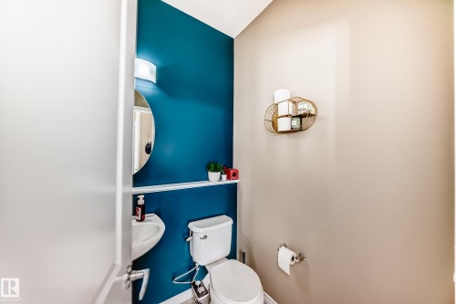 Powder room featuring a wall-mounted sink, round mirror, and a wall-mounted light fixture - 5020 Orchards Gate, Edmonton, AB - Indoor Photo Showing Bathroom