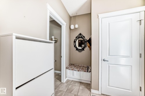 Entryway featuring tile flooring, a built-in storage bench, a decorative mirror, and a modern pendant light fixture - 5020 Orchards Gate, Edmonton, AB - Indoor Photo Showing Other Room