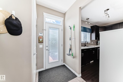 Entryway with a glass-paneled door and a kitchen featuring dark wood cabinetry, a tiled backsplash, a black faucet, and track lighting - 5020 Orchards Gate, Edmonton, AB - Indoor Photo Showing Other Room