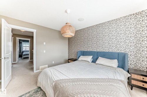 Bedroom featuring a patterned accent wall, plush carpeting, a modern pendant light fixture, and a built-in ceiling speaker - 5020 Orchards Gate, Edmonton, AB - Indoor Photo Showing Bedroom