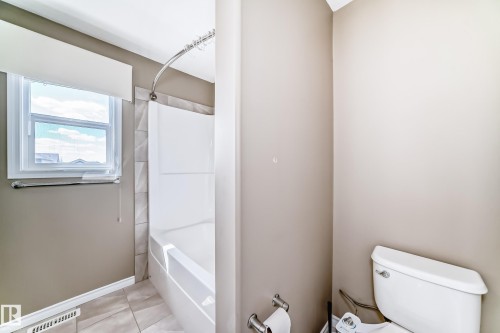 Bathroom featuring a white bathtub, ceramic tile surround with geometric pattern, chrome curved shower rod, and a window with white trim - 5020 Orchards Gate, Edmonton, AB - Indoor Photo Showing Bathroom