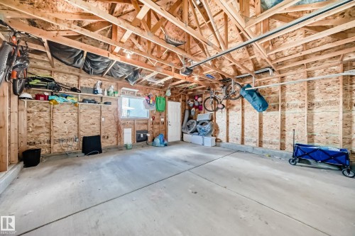 Spacious garage with exposed wood framing, concrete flooring, built-in shelving, overhead lighting, and a single window for natural light - 5020 Orchards Gate, Edmonton, AB - Indoor Photo Showing Garage