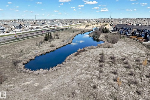Expansive undeveloped land featuring a meandering water body with natural vegetation, bordered by residential development and a paved roadway - 5020 Orchards Gate, Edmonton, AB - Outdoor With View