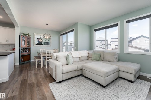 Open-concept living area featuring wood-finish flooring, ample natural light through multiple windows, a geometric pendant light fixture, and a built-in cabinetry unit - 1450 Darby Green, Edmonton, AB - Indoor Photo Showing Living Room