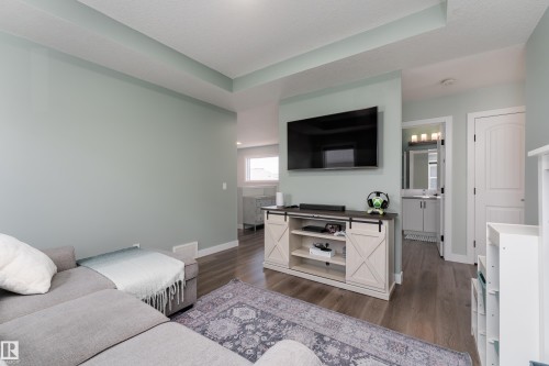 Living area featuring wood-finish flooring, recessed ceiling detail, and a built-in media console with barn door-style accents - 1450 Darby Green, Edmonton, AB - Indoor Photo Showing Living Room