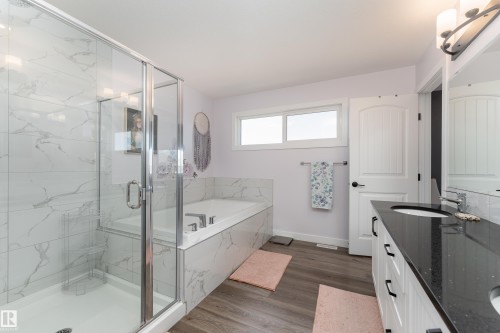 Spacious bathroom featuring a glass-enclosed shower with subway tile surround, a built-in tub with matching tile, dual vanity with a dark countertop and undermount sinks, and wood-finish flooring - 1450 Darby Green, Edmonton, AB - Indoor Photo Showing Bathroom