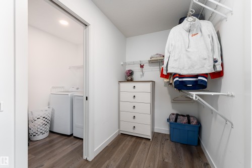 Walk-in closet with wood-finish flooring, built-in wire shelving, and a pocket door leading to a laundry area with a washer and dryer - 1450 Darby Green, Edmonton, AB - Indoor