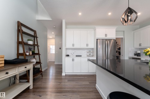Kitchen featuring white shaker-style cabinetry, a large kitchen island with a black countertop, stainless steel refrigerator, recessed lighting, and wood-finish flooring - 1450 Darby Green, Edmonton, AB - Indoor Photo Showing Kitchen With Stainless Steel Kitchen With Upgraded Kitchen