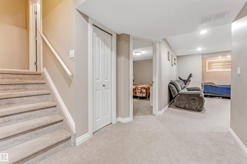 Carpeted staircase with white handrail leading to a lower level featuring neutral wall tones, recessed lighting, and a white bi-fold closet door - 3236 26 Avenue, Edmonton, AB - Indoor
